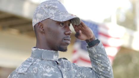 serious african american male soldier saluting with flag in background on sunny day, slow motion