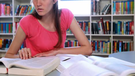 Attentive-schoolgirl-doing-homework-in-library