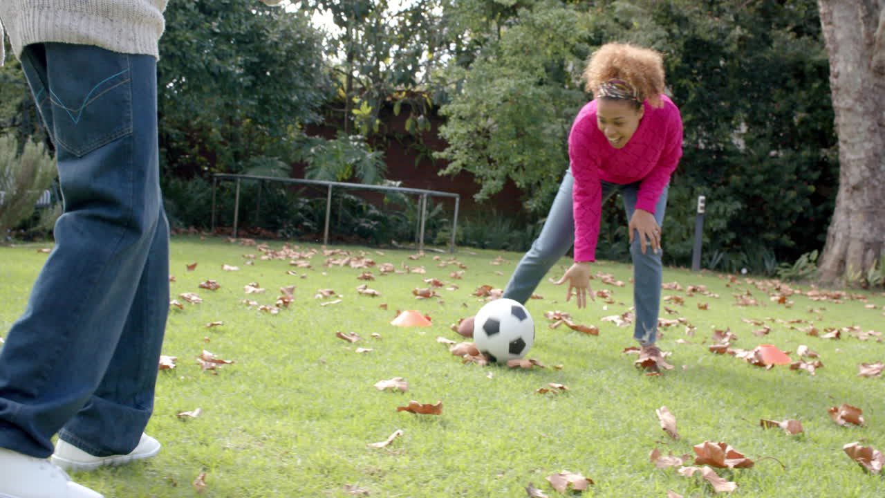 Happy african american mother and son playing football and embracing in garden, slow motion