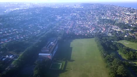 Drohnenaufnahmen-über-Dem-Bluff-Golfplatz-Mit-Der-Grosvernor-Boys-High-School-In-Der-Ferne-Und-Sich-Bewegenden-Menschen-Und-Autos-Auf-Einer-Straße