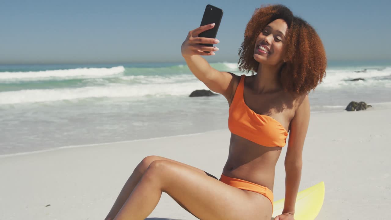 mujer afroamericana sentada en su tabla de surf tomando una selfie