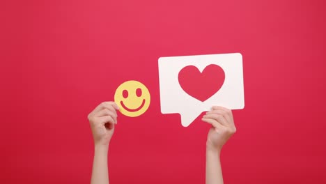 cerca de las manos femeninas sosteniendo icono de reacción compartir repost comentario popular hacer clic y pequeña cara sonriente amarilla feliz, buena retroalimentación, aislado en la pared de fondo de estudio rojo. blogger y concepto en línea