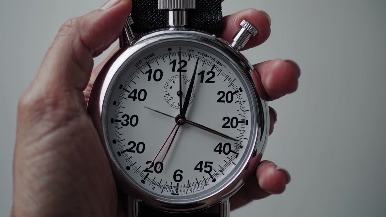 Close-up video of a hand holding a stopwatch, angled slightly from above, capturing the concept