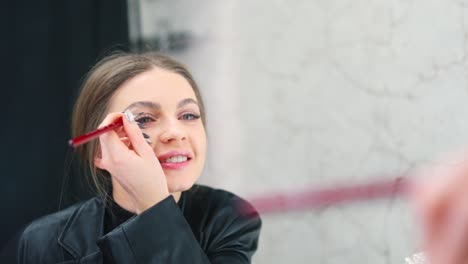 young woman applying eyebrow makeup in front of a mirror