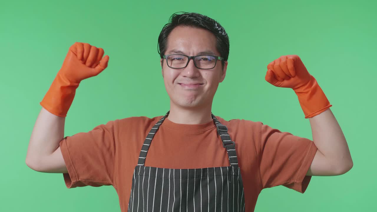 녹색 스크린 스튜디오에 서 있는 동안 그녀의 비셉스를 보여주는 아프론을 입은 아시아 남성 집사.