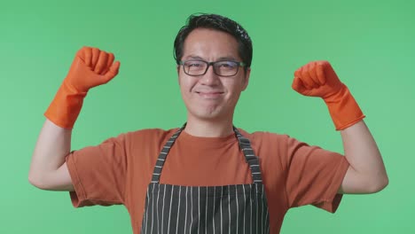 primer plano de una ama de casa asiática con un delantal mostrando sus bíceps mientras estaba de pie en el estudio de pantalla verde