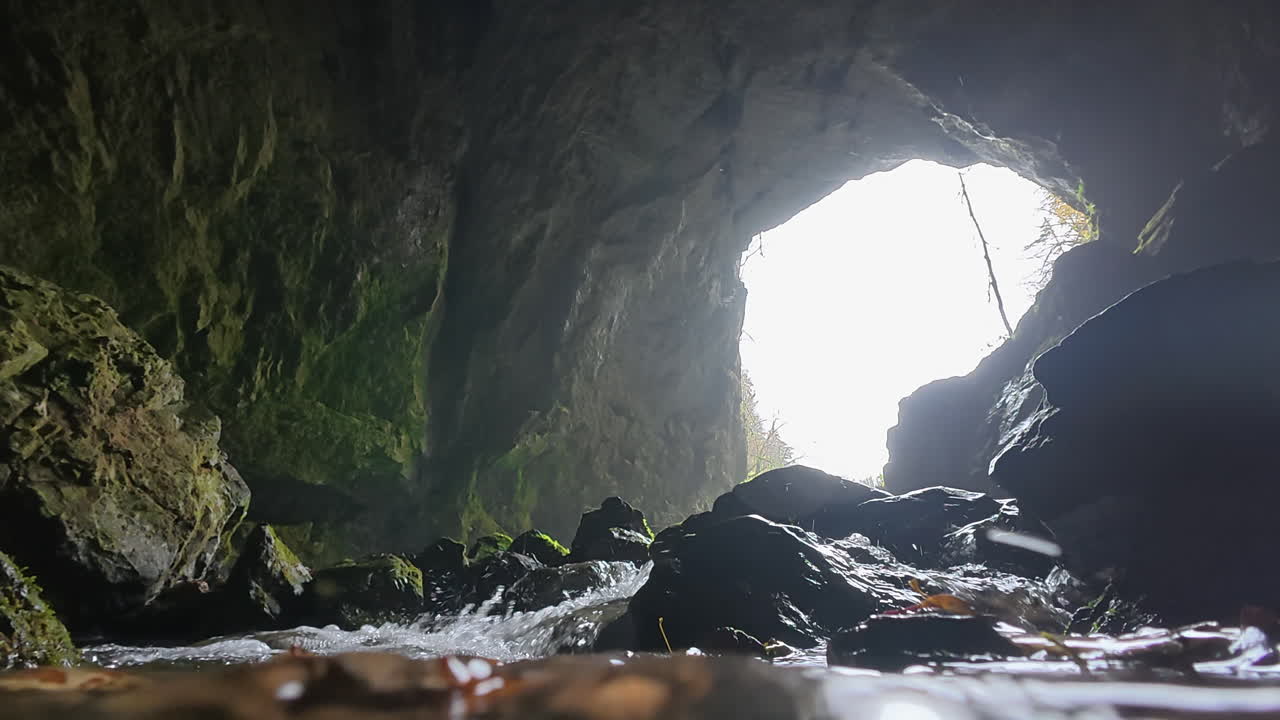 Tkalca Cave: Stunning low angle shot of a clear mountain river flowing out of a dark cave into the sunlight