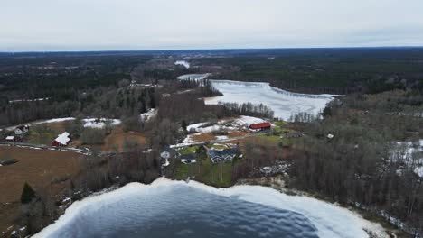 Beautiful aerial of Swedish homes at the shore of a large frozen lake in rural Sweden