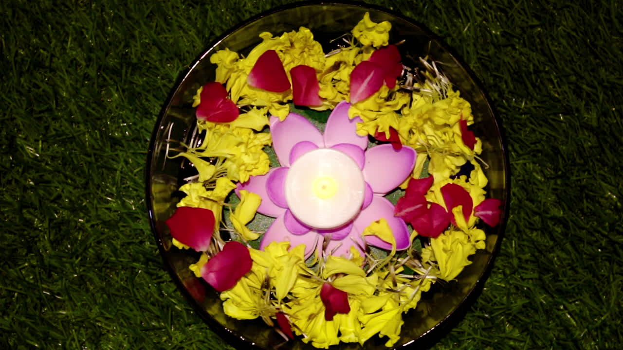 India flower bowl decoration with candle light for Diwali festival and prayer celebration, yellow and pink petals arranged in round bowl on grass creating festive and peaceful mood