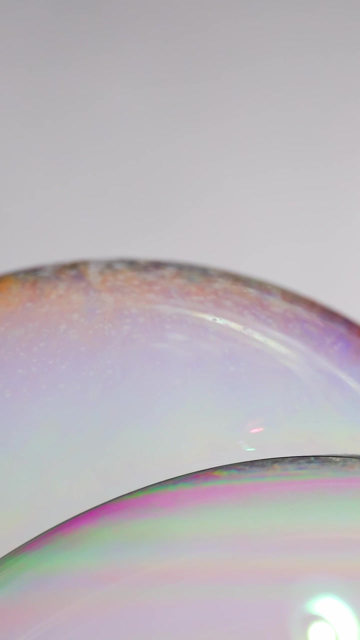 Close-up of soap bubble with shifting colors under soft lighting, capturing delicate surface reflections