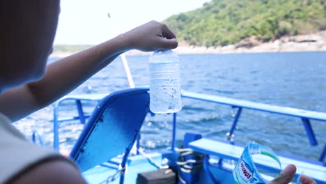 una persona quita una etiqueta de una botella de agua mientras disfruta de un paseo panorámico en barco en phuket, tailandia