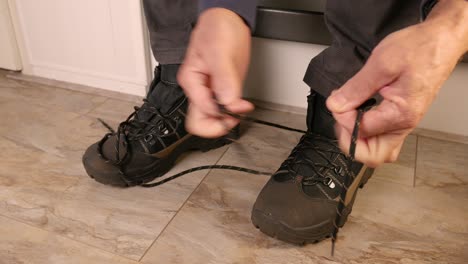 a man sitting on the stairs in the hallway laces up his walking shoes