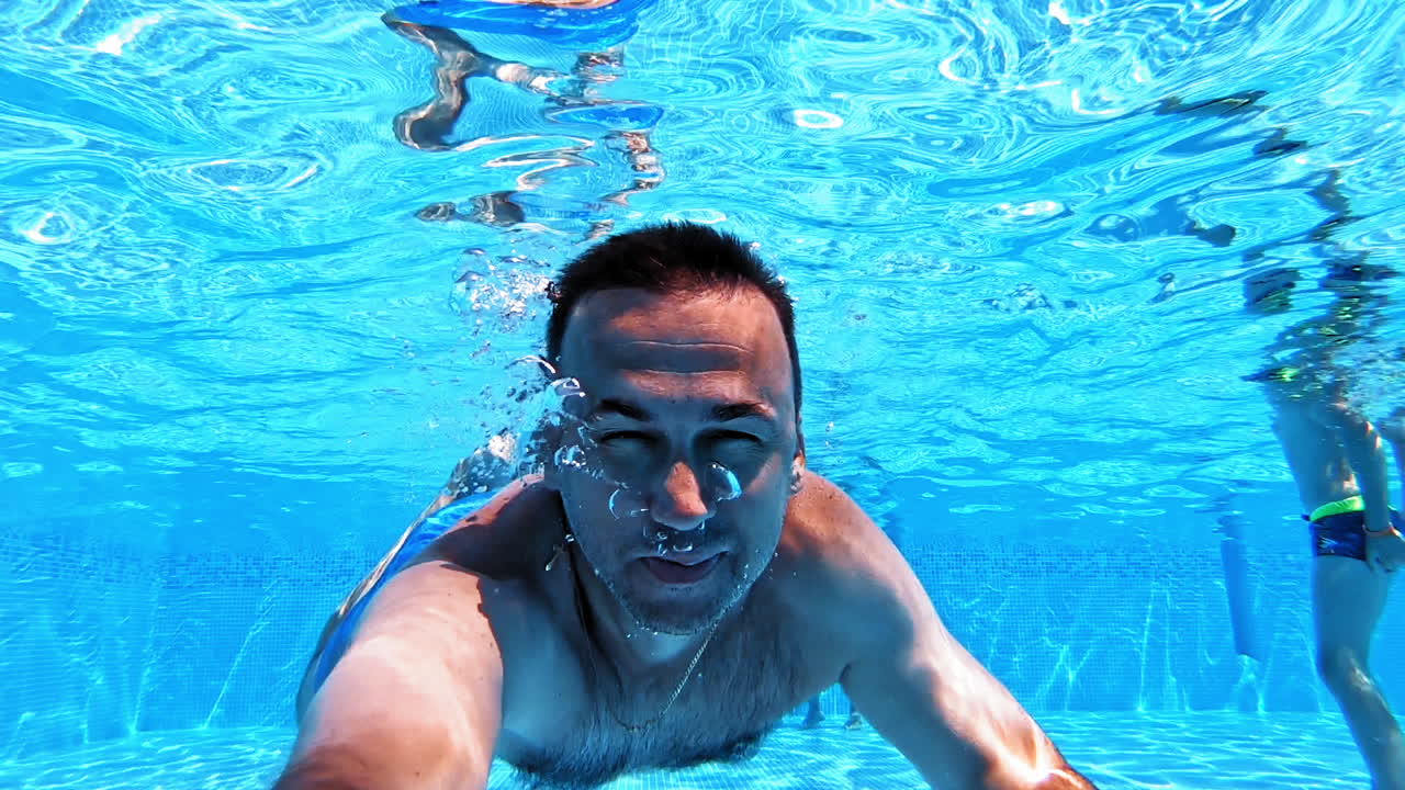 Man swims underwater in the pool. Blue clear water and a male swimming ahead with underwater camera. Summer vacation at water.
