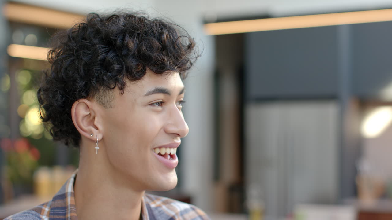 Smiling young man with curly hair and earrings in modern home setting, copy space