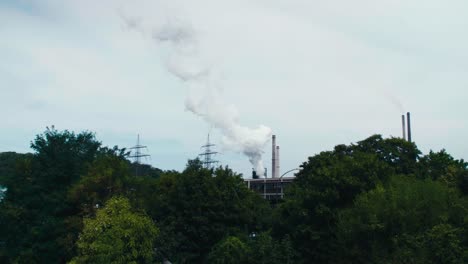 Wide-cinematic-shot-of-energy-plant,-smoke-going-up,-shot-with-trees-in-the-foreground