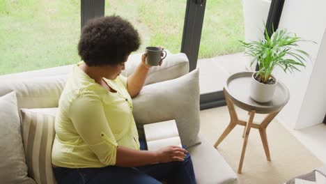 Video-Einer-Afroamerikanerin-In-Übergröße,-Die-Mit-Kaffee-Und-Laptop-Auf-Dem-Sofa-Sitzt