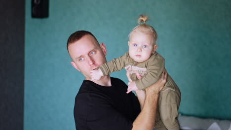 man is holding his little child in front of him. dad making faces to a kid and entertains the baby.