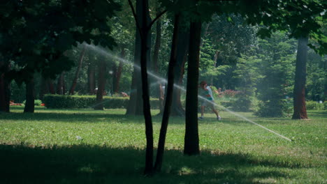 playful little boy running water sprinkles in green park hiding ears from splash