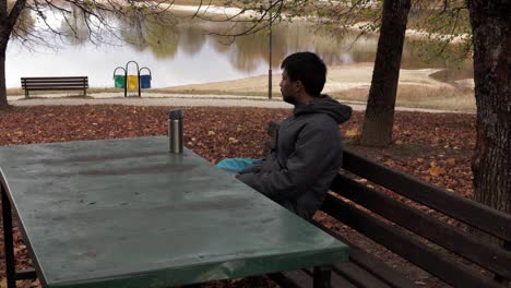 Amidst-autumn's-allure,-a-man-enjoys-tea-on-a-park-bench,-embracing-the-gentle-rustle-of-leaves