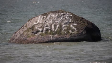 hand painted rock in sea bears message “jesus saves”, slow motion scene