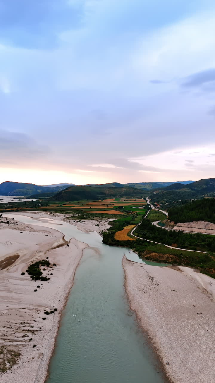 Picturesque landscape of Albania from top view. Drone footage over the narrow river with sandy banks. Rare cars go by the highways in the mountains. Vertical video.
