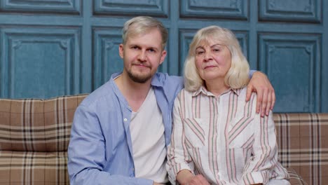 a mother and son smile for the camera, sitting together on a couch.