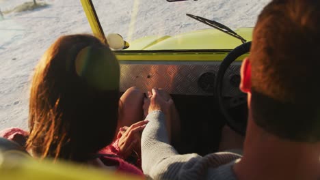 Happy-caucasian-couple-sitting-in-beach-buggy-by-the-sea-hugging