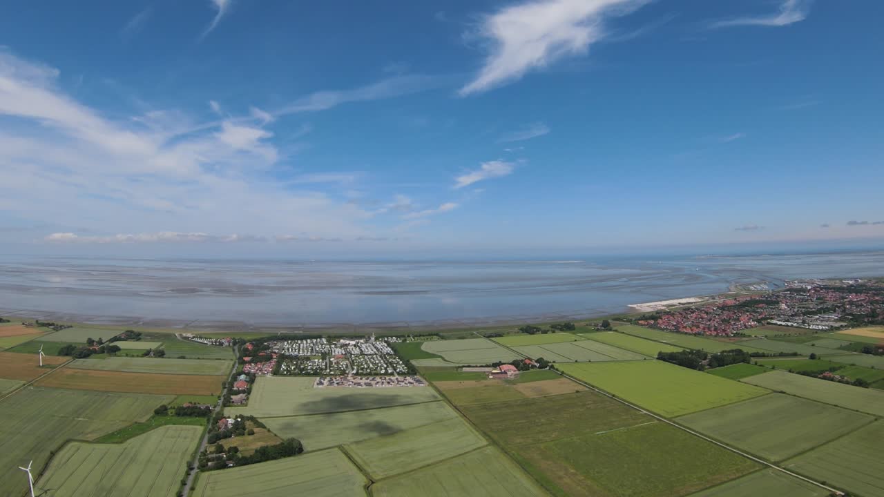 aerial shots of a wide, flat coast with a small village and many fields and a cloudy sky