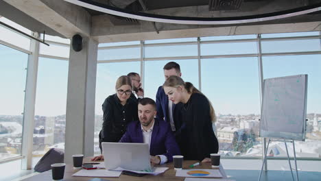 group of colleagues stand around the boss with a laptop. other businessman has a telephone conversation. team working in a spacious office.