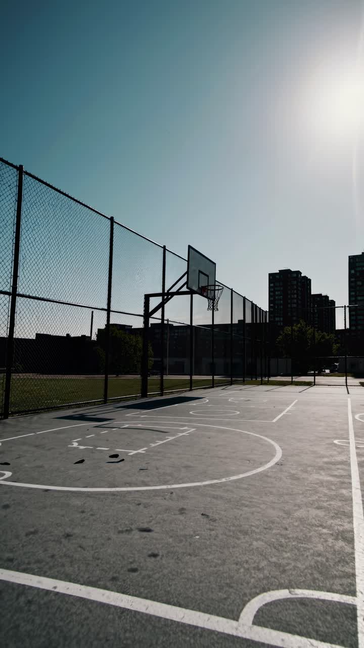 Low-angle shot of an empty urban basketball court under a clear sky, creating a serene, cinematic