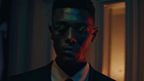 Businessman wearing glasses stands in a dark room, illuminated by vibrant, colorful lights. Shadows dance around, creating a mysterious and dramatic atmosphere full of intrigue