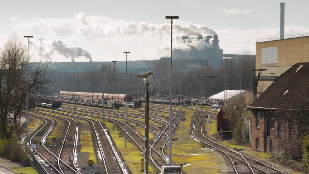 바쁜 철도 야드 에 주차 된 화물 열차 는 산업 공장 들 과 함께 배경 에 연기 를 방출 한다.