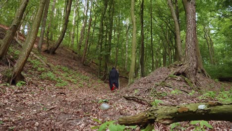 rear view of a grim reaper in black hooded cloak clutching a scythe walking in the forest