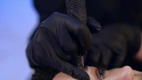 tattooist's gloved hands use machine for eyebrow permanent. make up at beauty salon. close up.