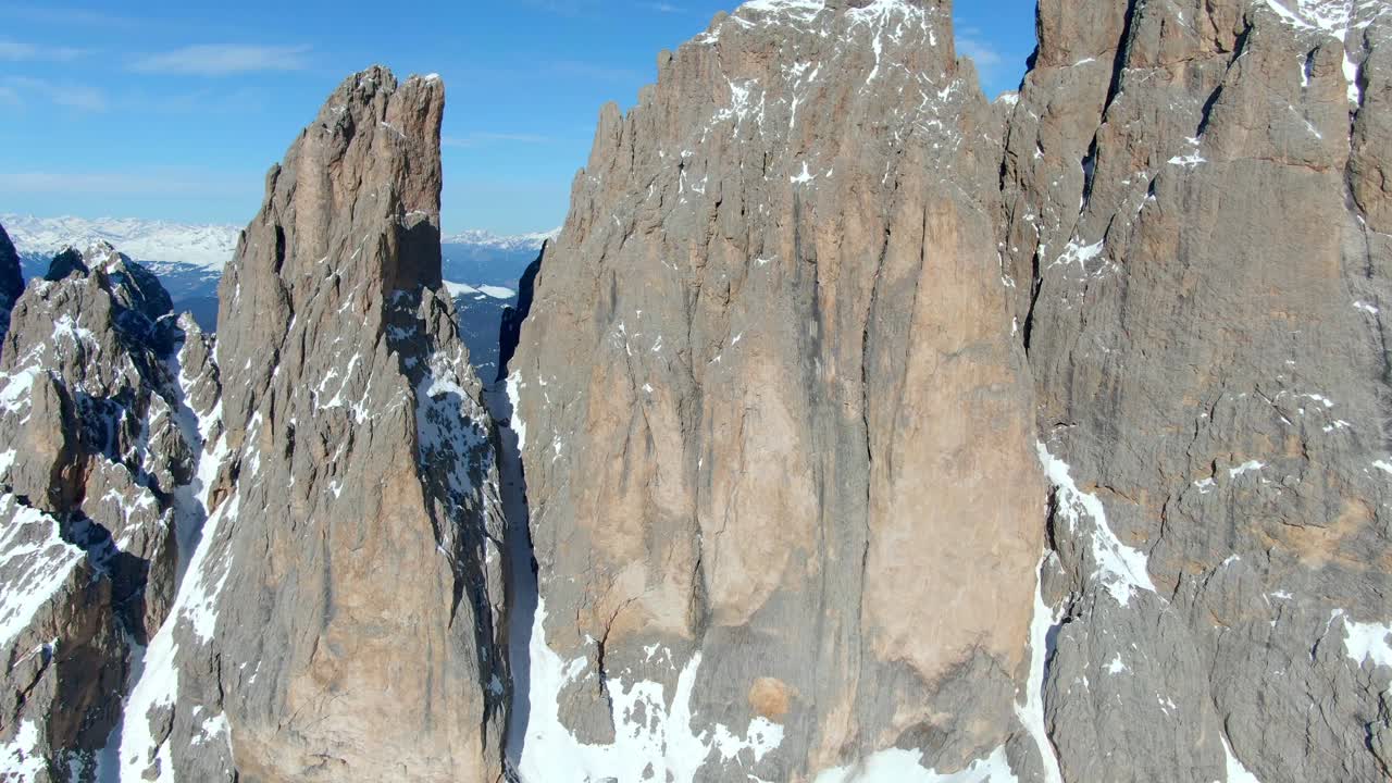 햇빛 아래 돌로미티의 정상에서 눈 덮인 파사 암석을 보여주는 서사시적인 드론 샷