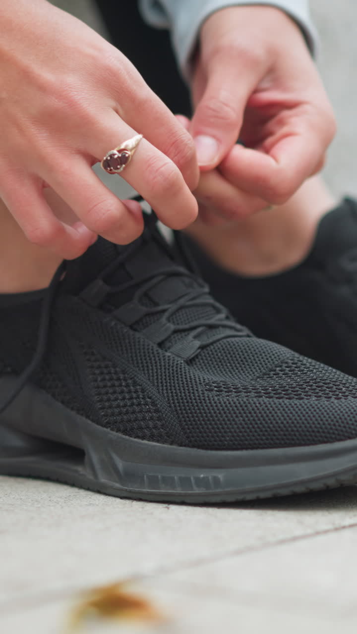 Primo piano di una ragazza sportiva che stringe un laccio nero sulle scarpe da corsa, preparandosi per l'allenamento fitness all'aperto, concentrata sulle calzature e sulla prontezza sportiva prima della sessione di allenamento.