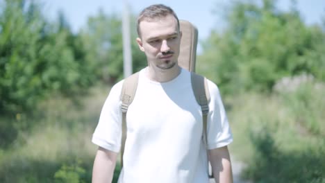 young man walking with guitar on street near forest