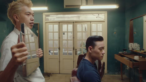 asian barber showing haircut to client with mirror