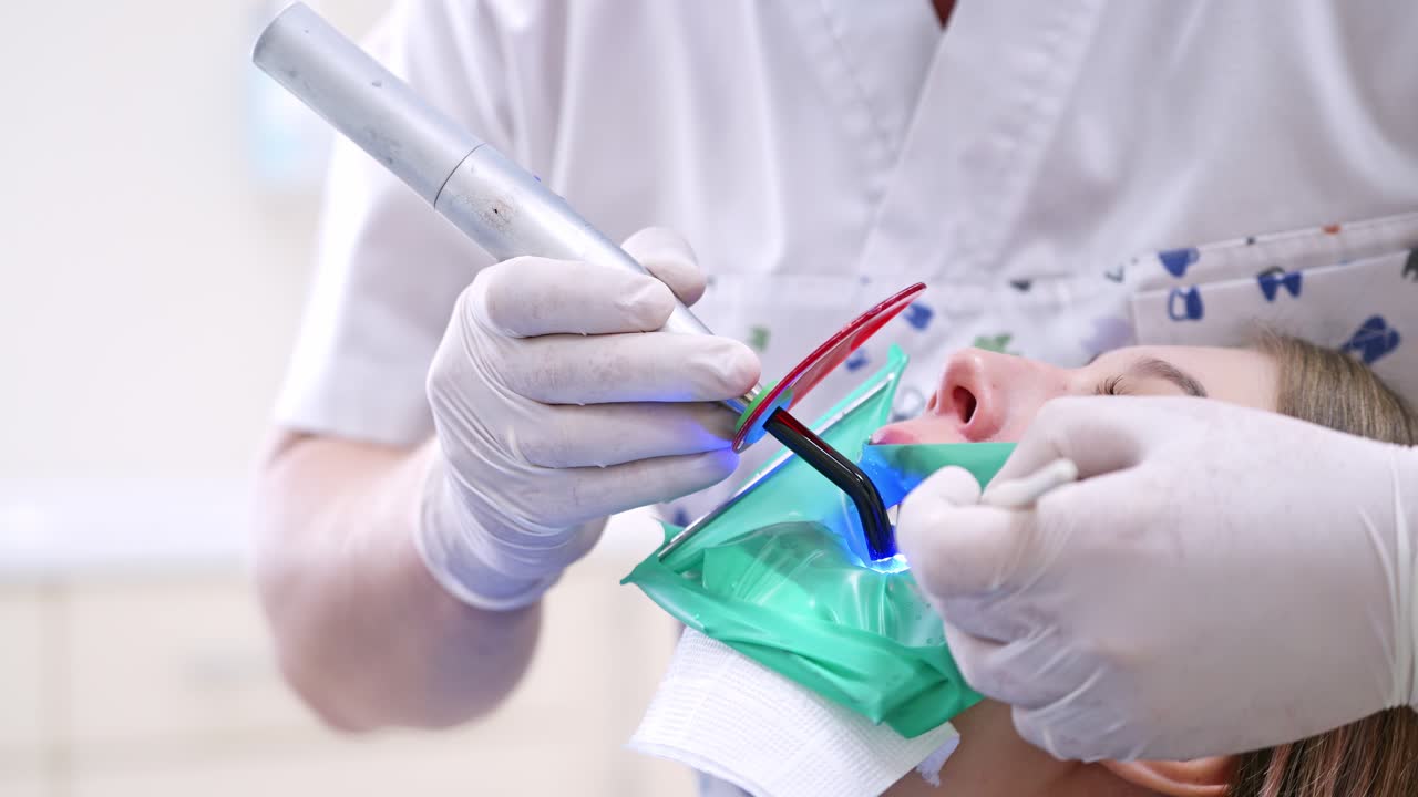 Doctor treats patient teeth in modern dental clinic. Photopolymer lamp in male doctor's hands.