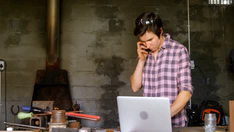 metalsmith talking on mobile phone while using laptop 4k