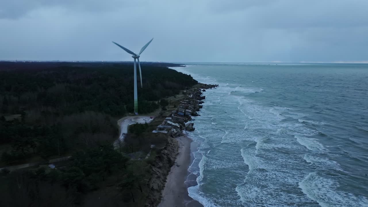 Historic Northern Fort ruins collapsing in sea beside modern wind turbine
