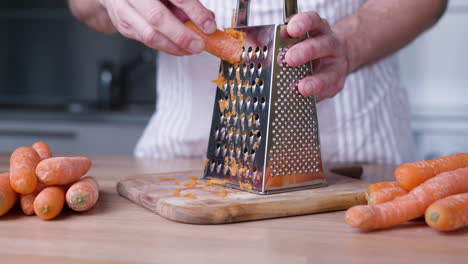 close up hand grating carrots on grater for carrot cake in the kitchen