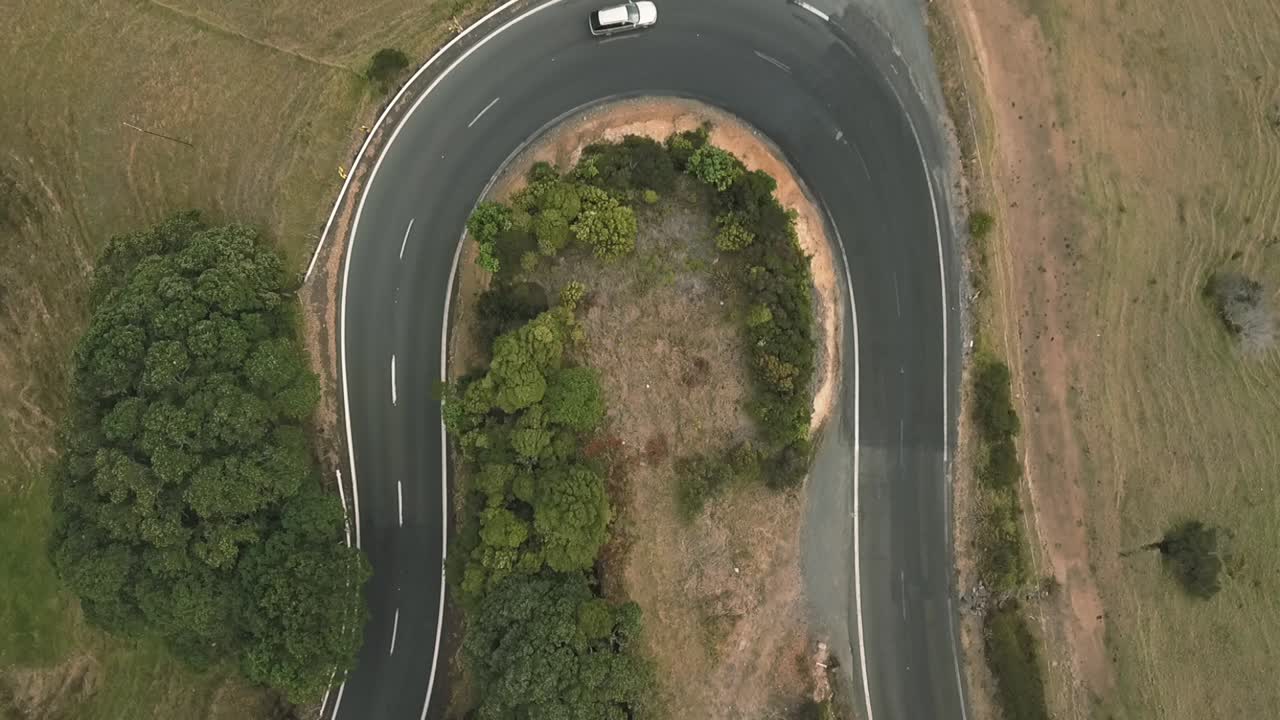 vista aérea de un dron a vista de pájaro de un coche blanco conduciendo por una carretera con curvas en las colinas de nueva zelanda