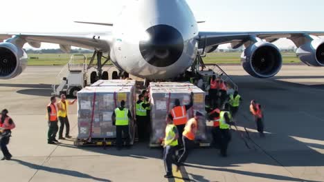 workers in high-visibility vests efficiently load large cargo onto a freight aircraft at the airport. the operation occurs in bright daylight, showcasing teamwork and logistics in action.