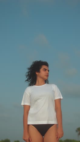 a confident woman standing on the beach with the wind blowing her hair