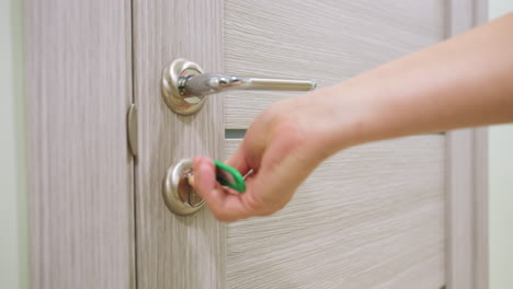young woman inserts key into modern silver lock unlocking wooden door and gently opening it with right hand showing everyday access routine at home or office representing security privacy entrance