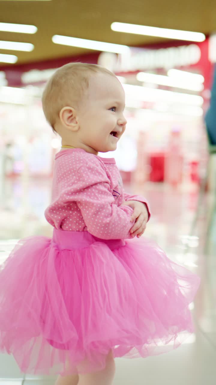 Bambina adorabile in un tutù rosa che esprime gioia in un ambiente luminoso e colorato, con giocosa sicurezza e fascino, catturata in due fotogrammi video