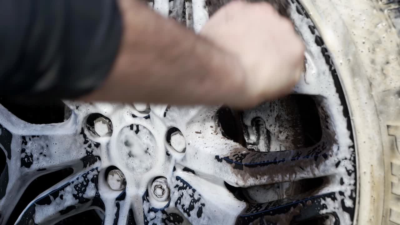 Close up cleaning black alloy wheels with barrel brush and lots of snow foam shampoo