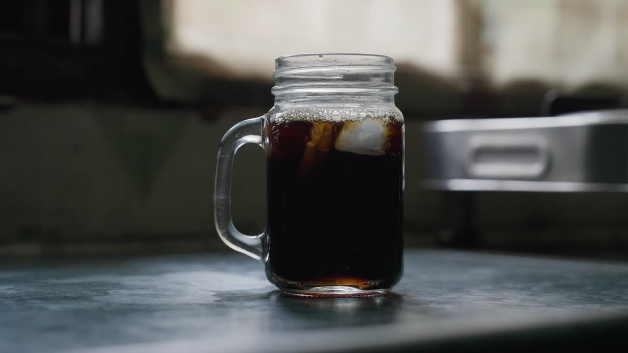A close-up footage of pouring the iced tea over the ice cubes in a glass cup on a kitchen counter