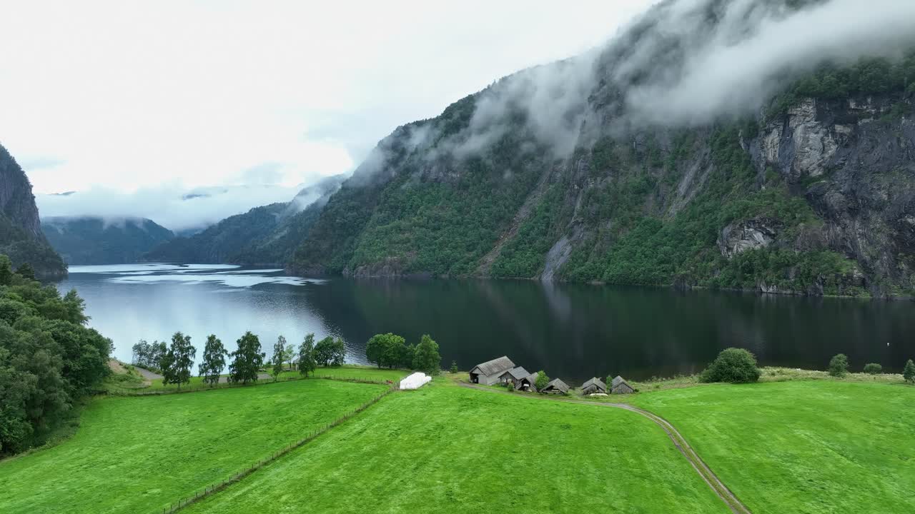 mañana idílica en el mar de bolstadfjorden en noruega - viejas casas de botes en la costa y altas montañas brumosas en el fiordo - movimiento lento hacia los lados de la escena aérea